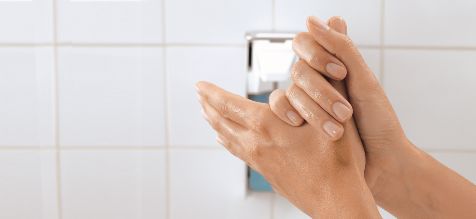 Disinfecting hands in front of a wall dispenser