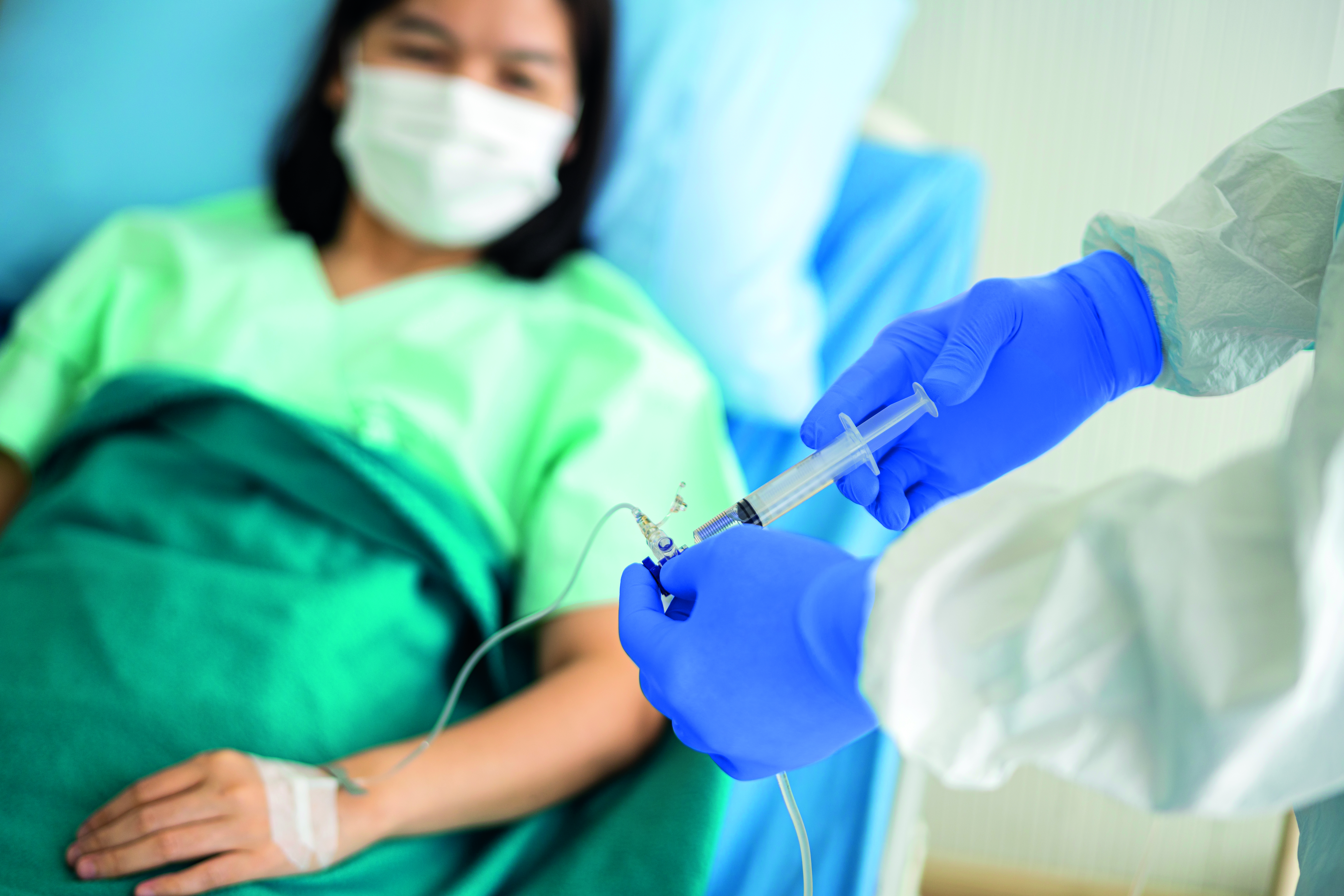 Asian female doctor in PPE medical suit and medical face mask in hospital with an injection vaccine and infusion drip for covid-19 or corona virus patient