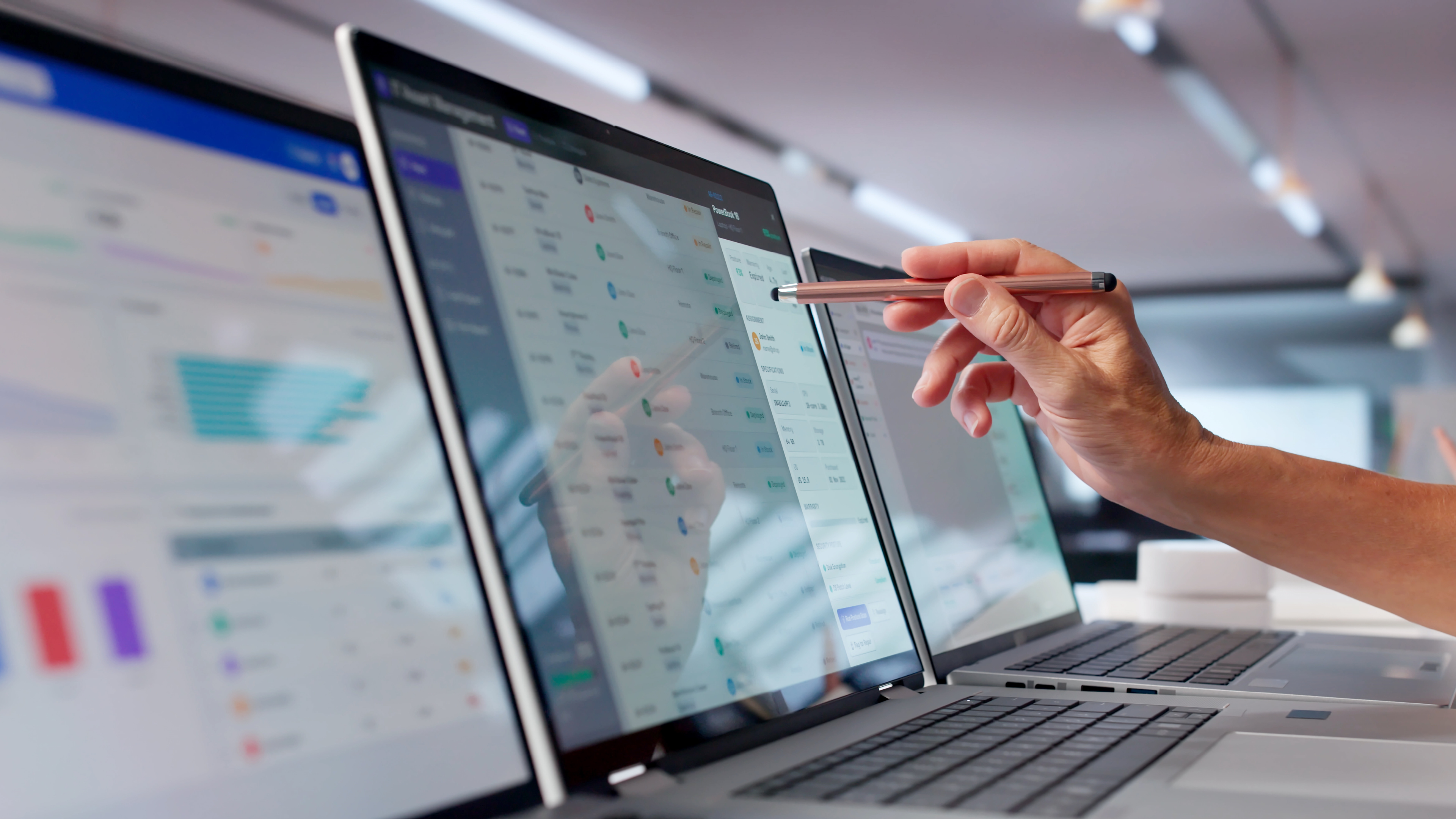 Hand interacting with data displayed on multiple laptop screens.