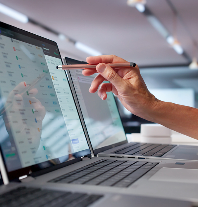 Hand interacting with data displayed on multiple laptop screens.