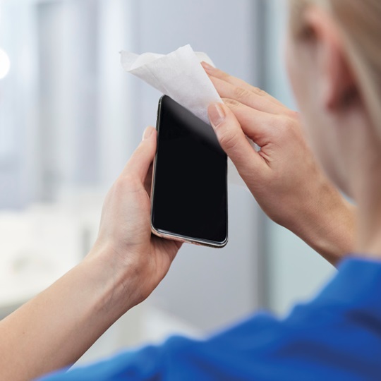 A woman disinfecting her mobile phone with the Sterillium surface spray