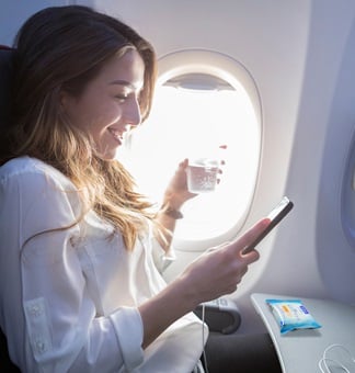 A woman sitting on a plane with a mobile phone in her hand and the Sterillium 2in1 wipes on the table in front of her.