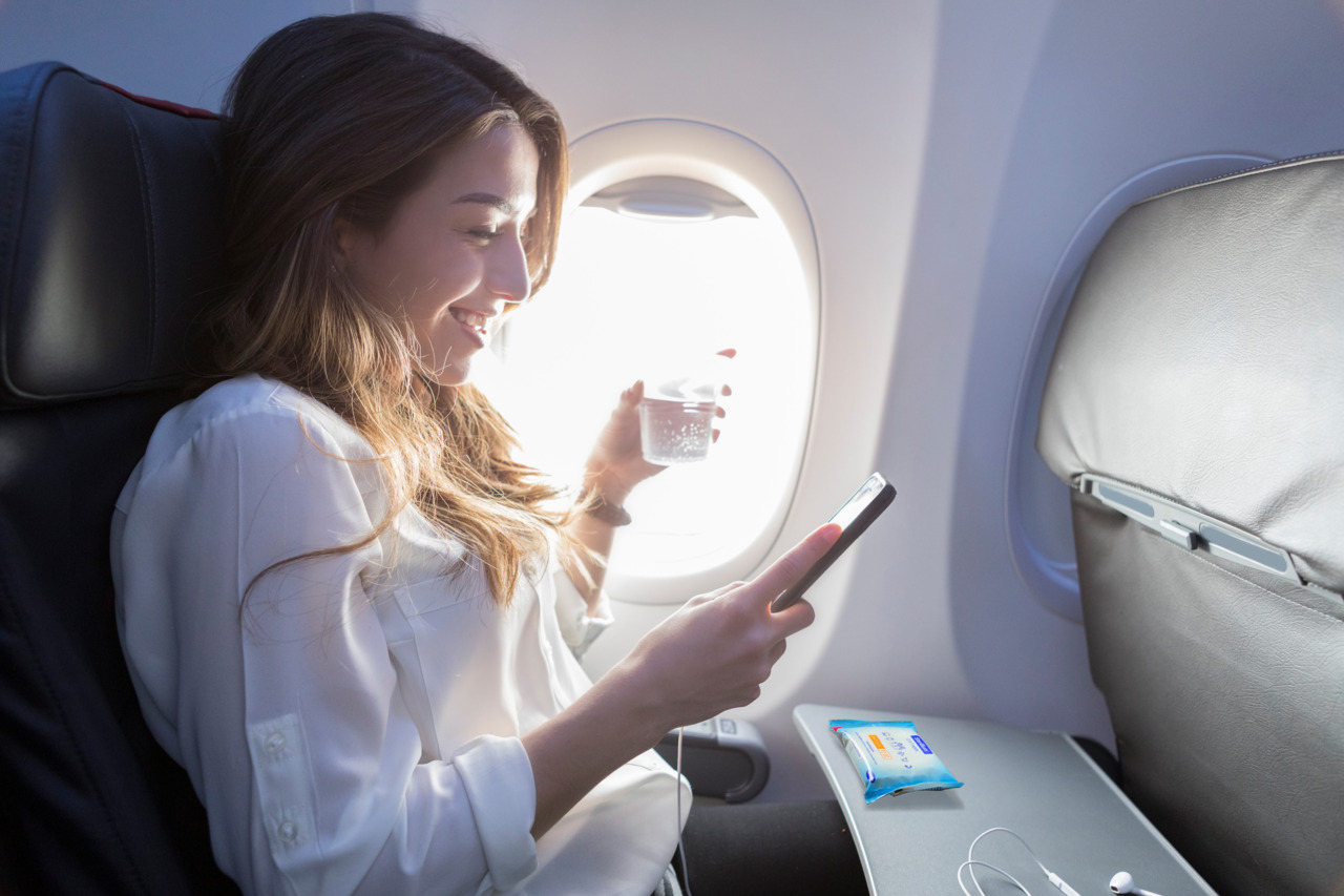 A woman sitting on a plane with a mobile phone in her hand and the Sterillium 2in1 wipes on the table in front of her.