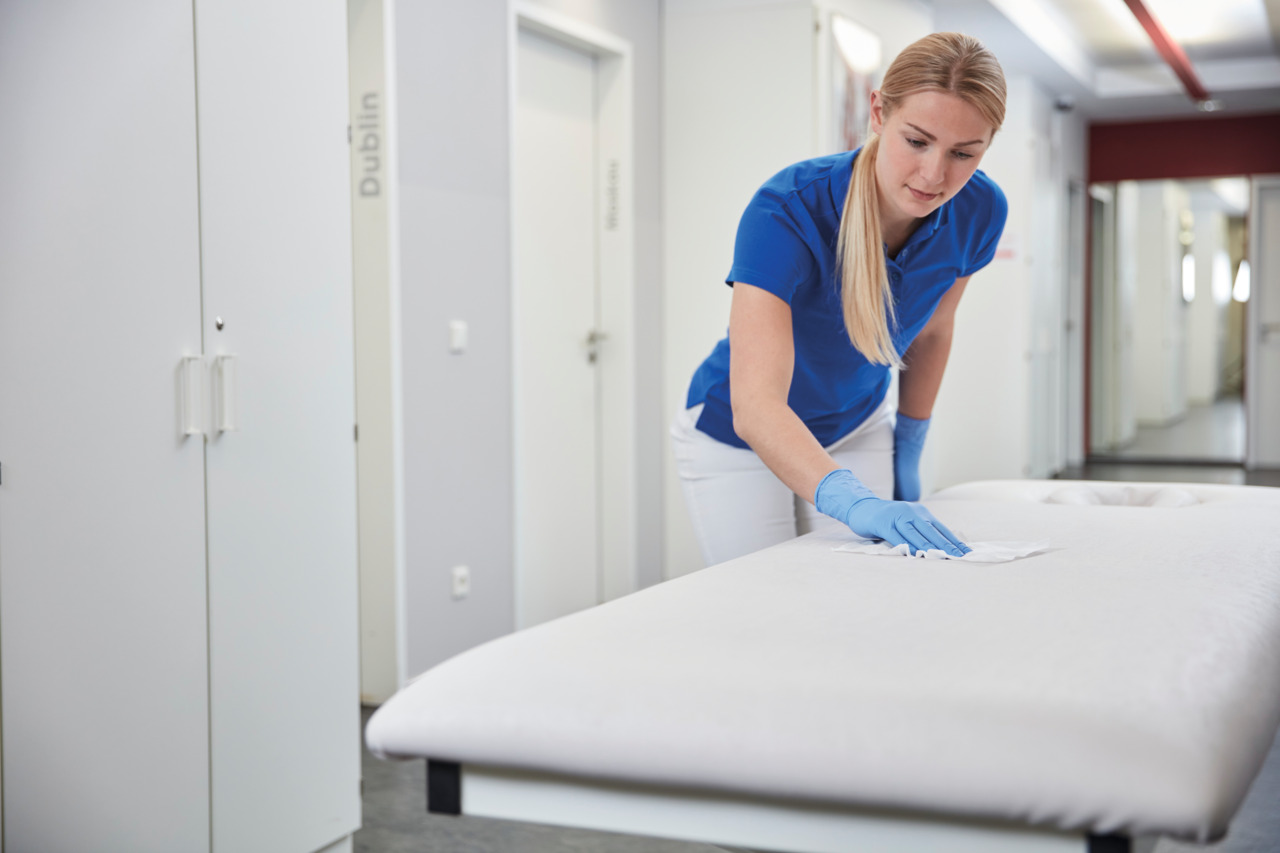 Female healthcare worker wearing gloves disinfecting a patient bed with disinfection wipes