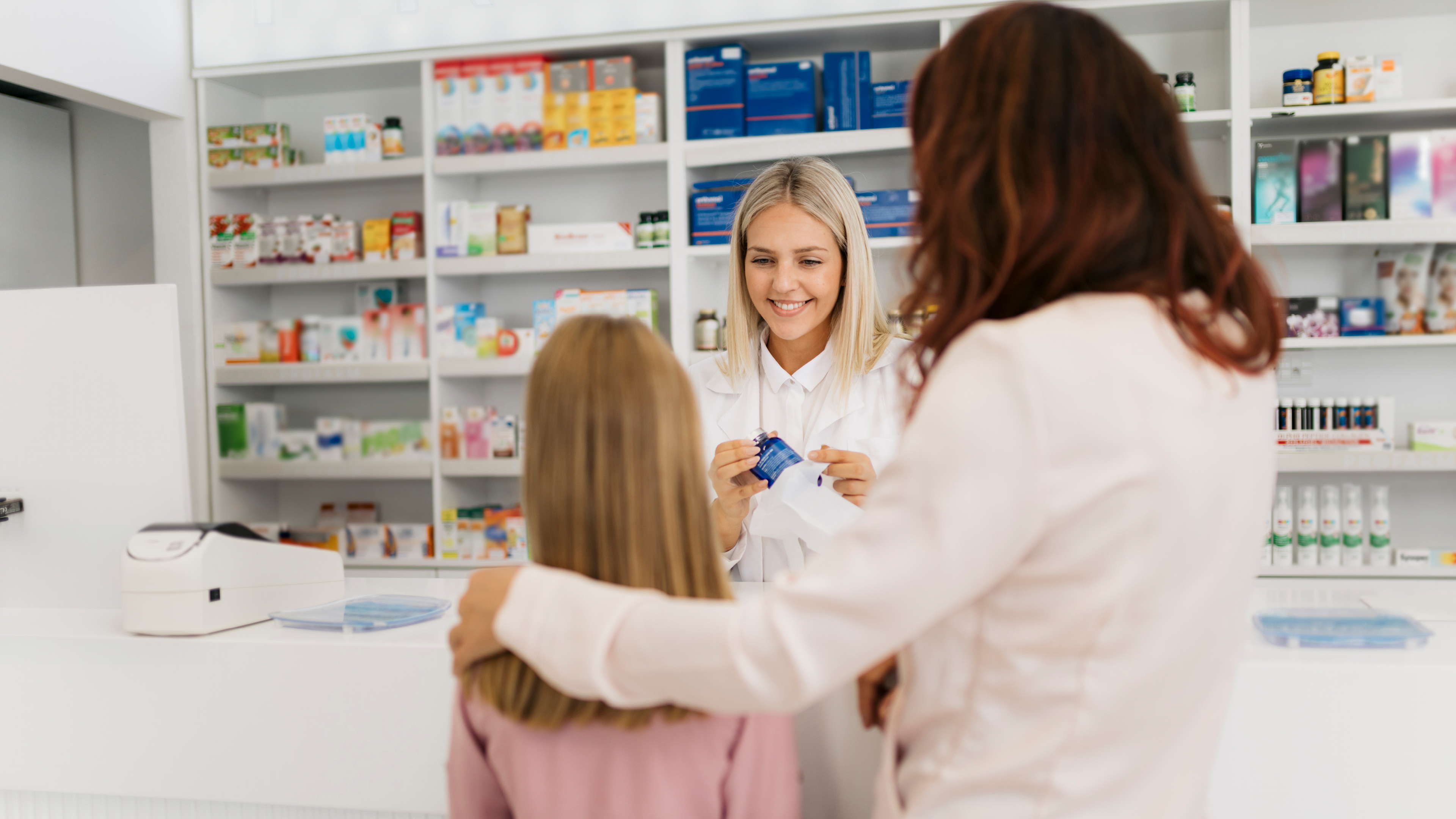 Sales situation in a pharmacy with a pharmacist and a mother with a child with shelves in the background