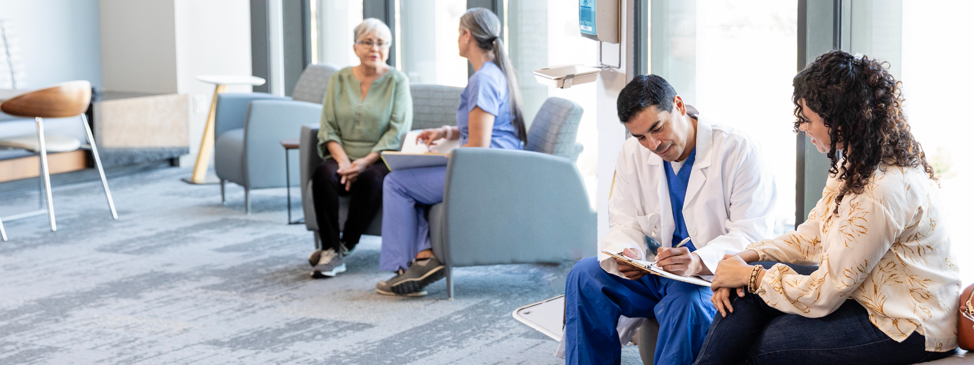 A hospital waiting area where doctors and patients sit in chairs