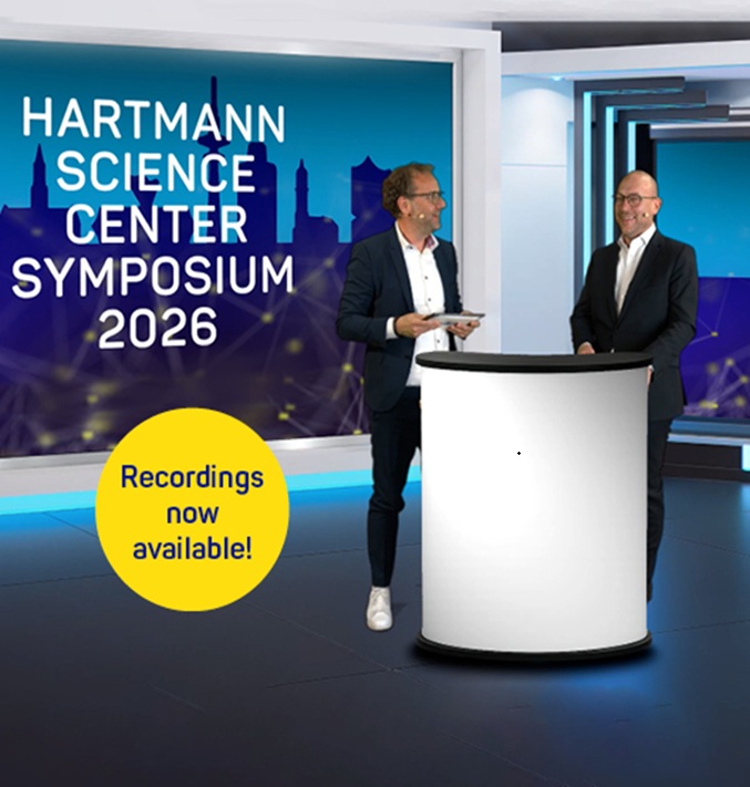 Two speakers with microphones standing behind a lectern bearing the text “HARTMANN SCIENCE CENTER Symposium 2026”
